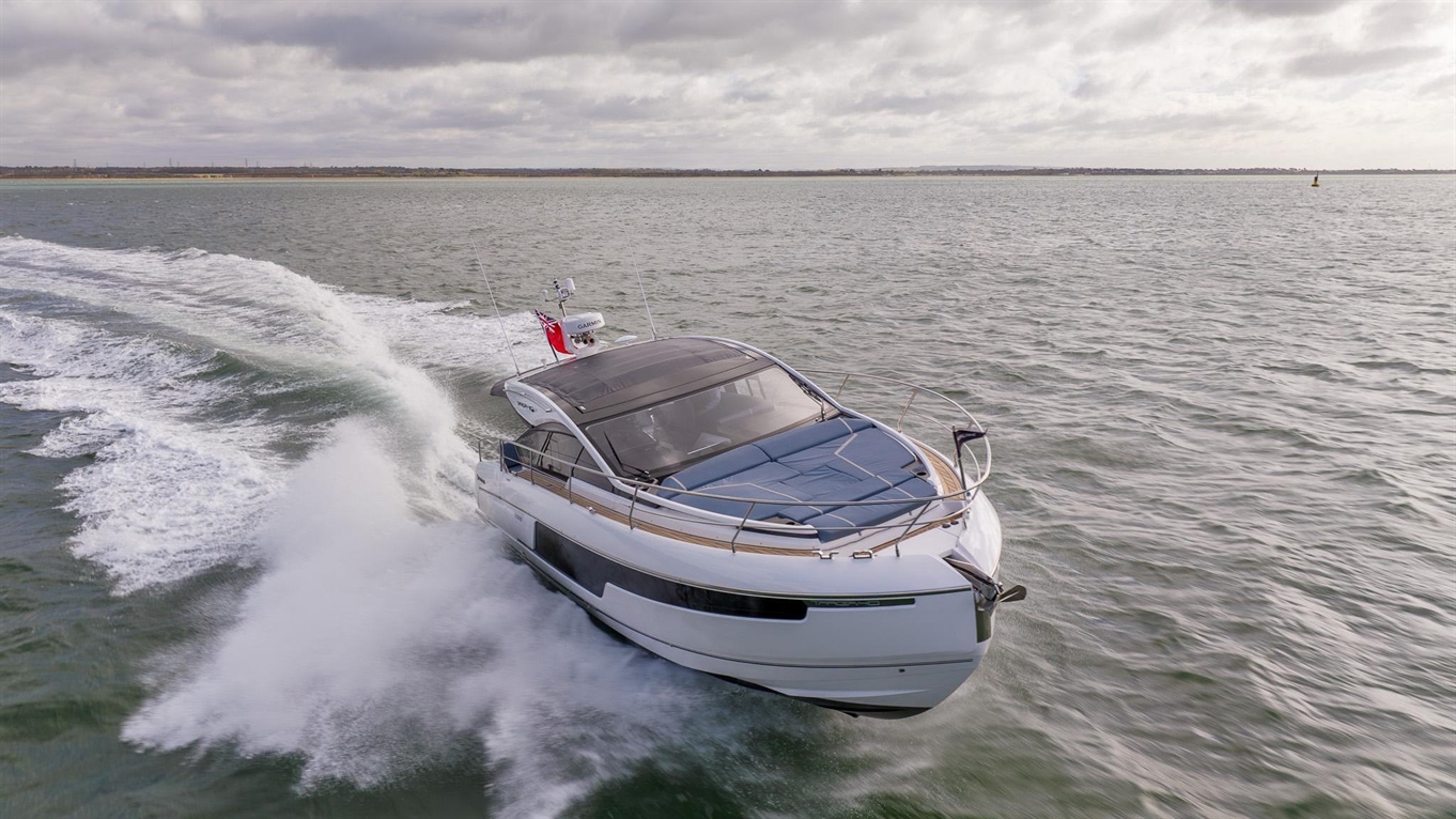 A luxury motorboat plows through waves on a calm sea, with a cloudy sky in the background, showcasing sleek design features.
